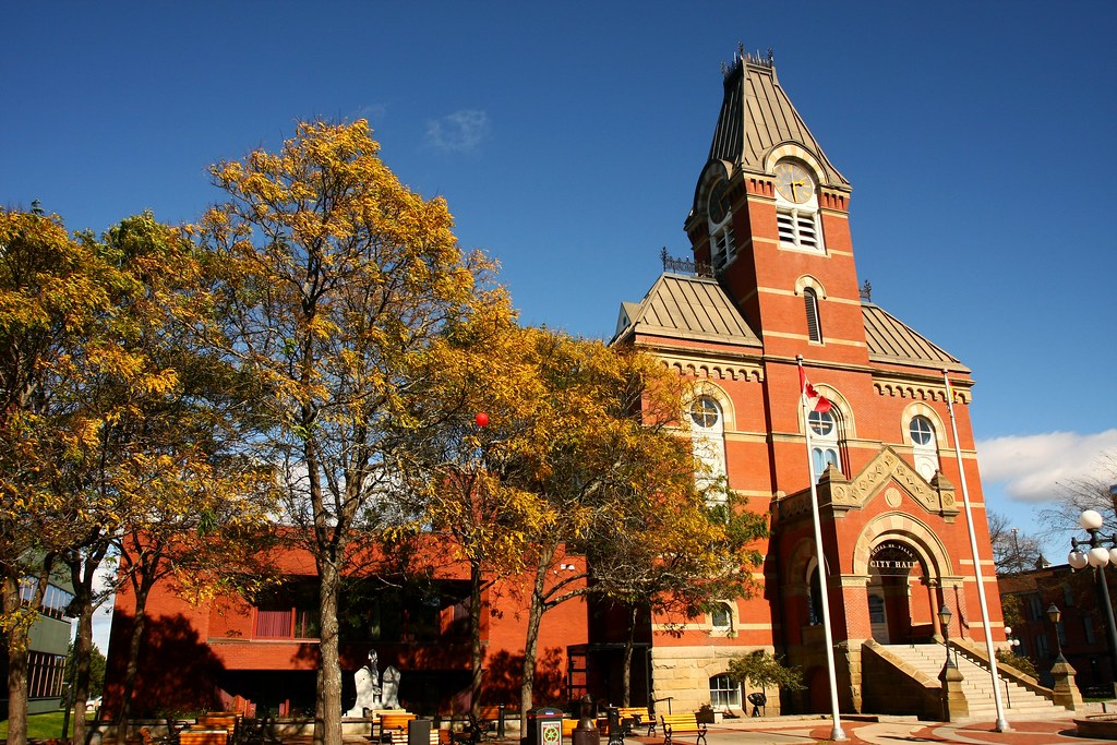 A photo of an orange brick building next to a tree that has browning leaves.